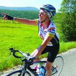 A biker pointing as she rides by a green field