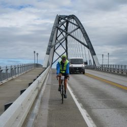 A cyclist rides across the Port Henry Bridge from New York to Vermont, with the SAG van following.