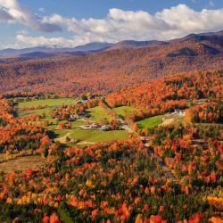 Brillian red and orange leaves blanket the hills surrounding farm land in rural Vermont